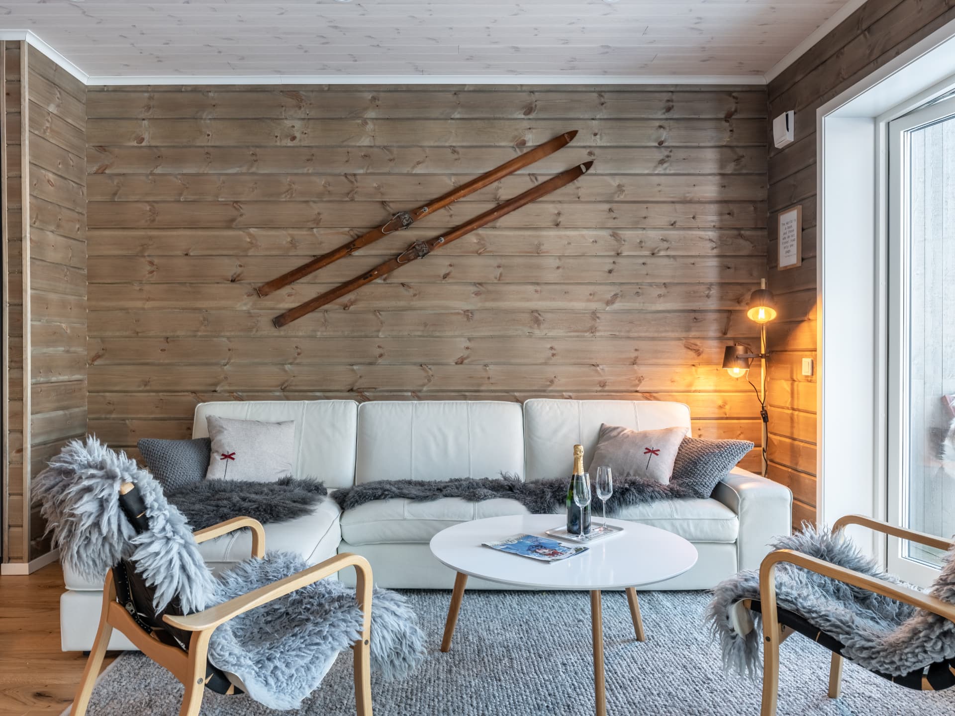Vardagsrum med vit soffa, fårskinn och antika träskidor på timmerväggen