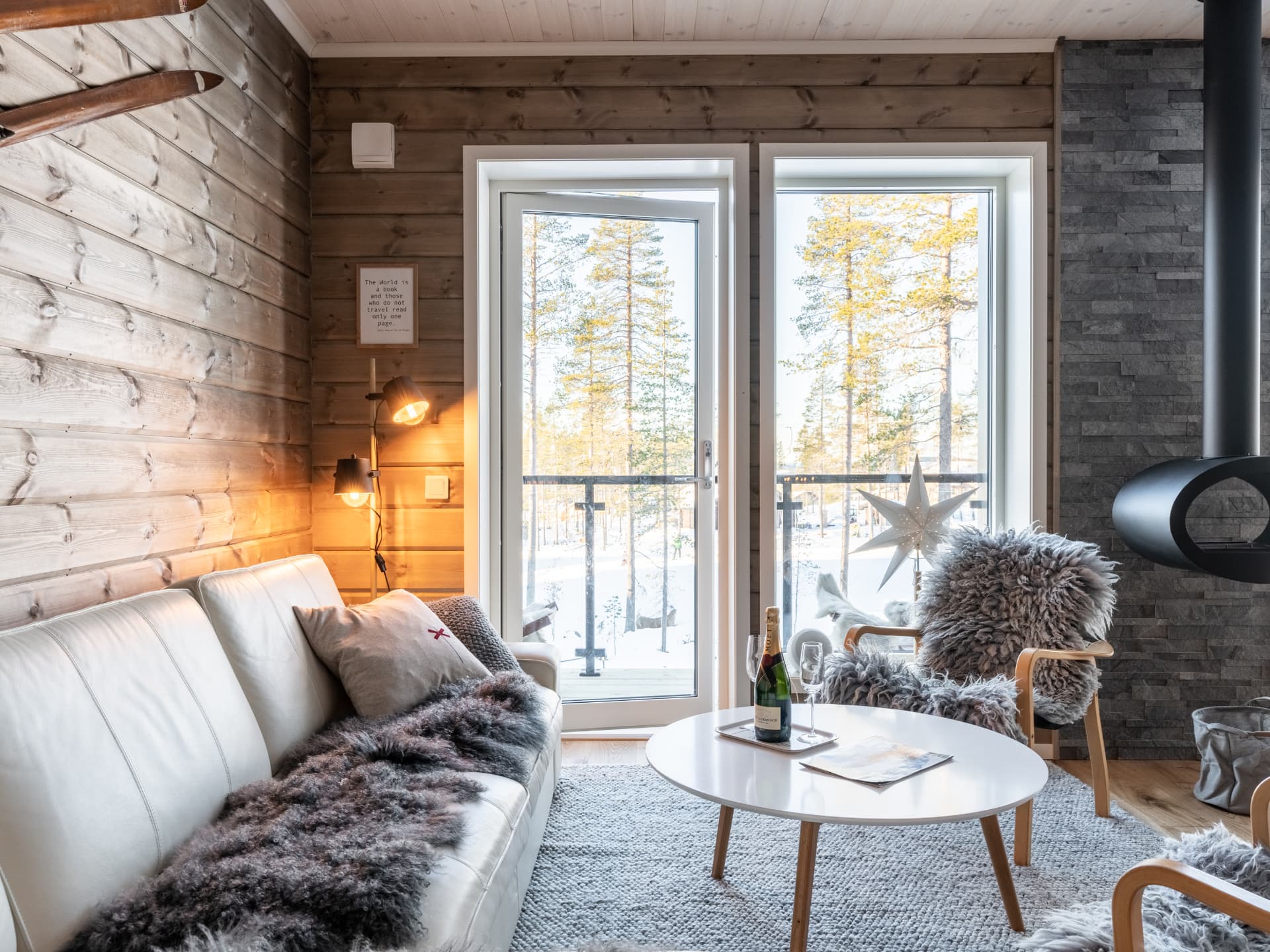 Vardagsrum med vit soffa, hängande braskamin och utsikt över snötäckta tallar