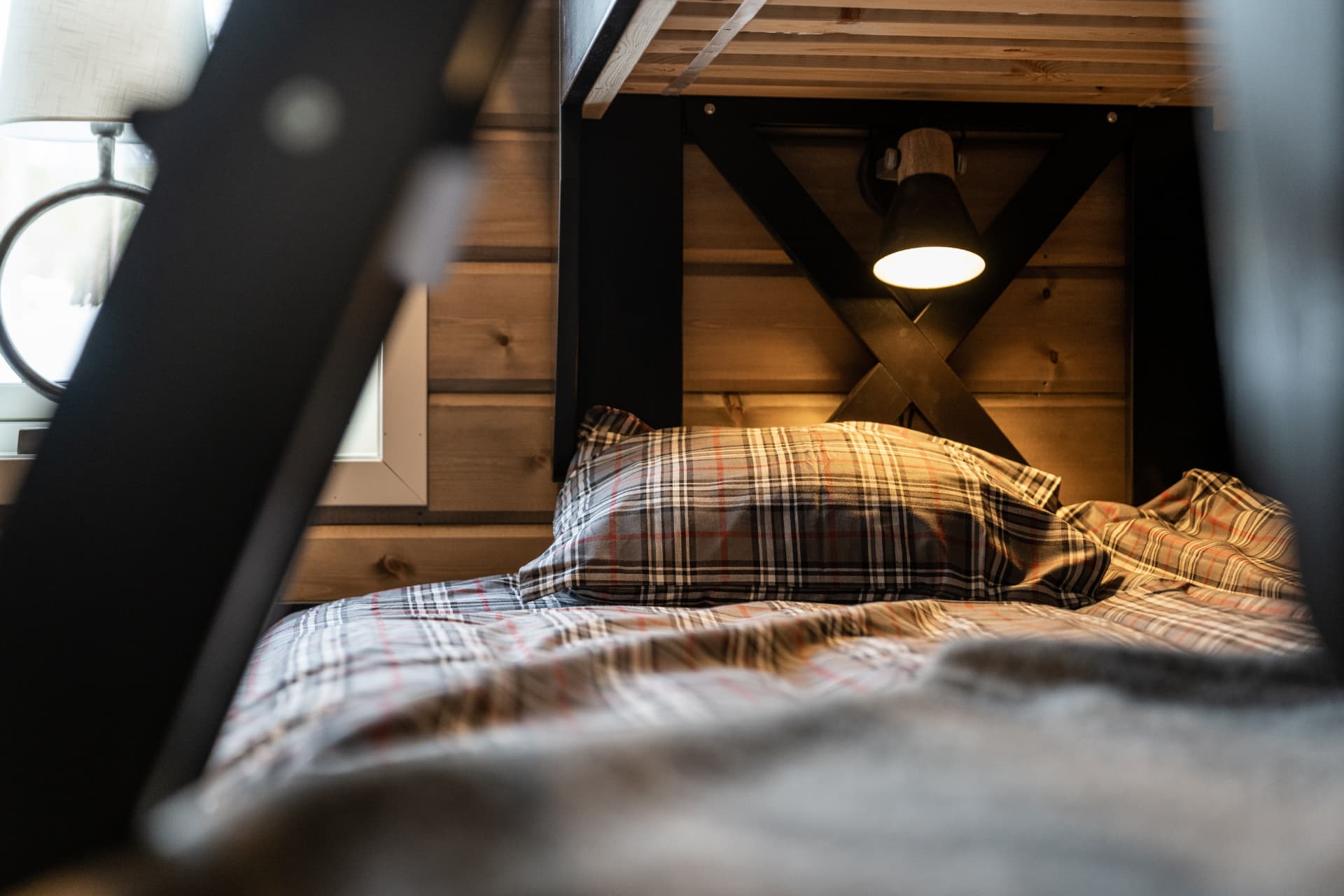 Sovrumsdetalj med rutigt sänglinne och tänd läslampa under våningssängen